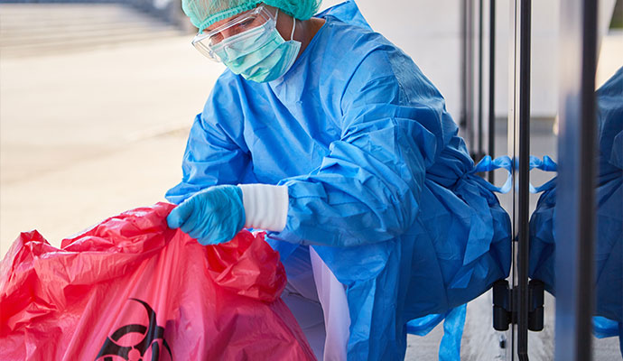 Person in PPE carrying hazardous waste in a biohazard bag