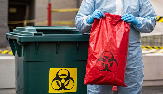 Worker holding red biohazard bag beside waste bin