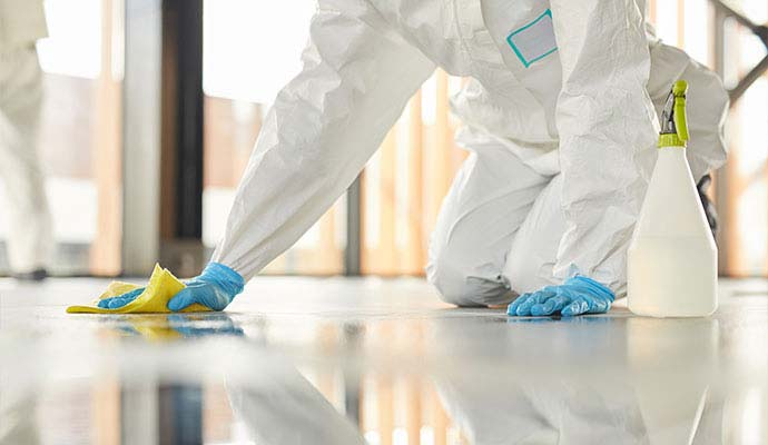 Technician in protective gear disinfecting a floor during blood cleanup and sanitation
