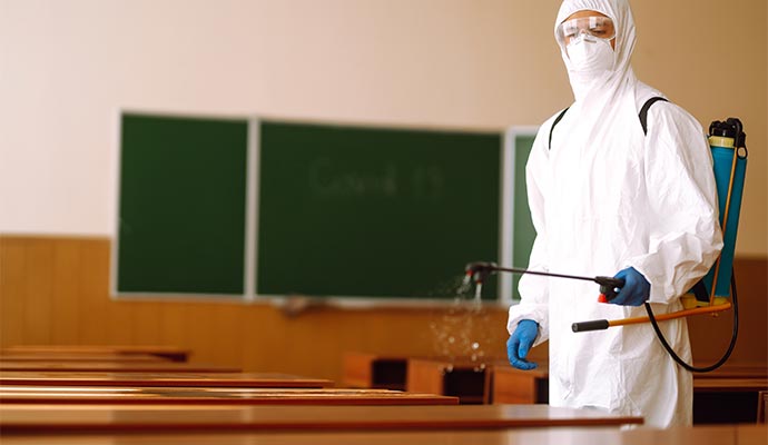 A professional is spraying disinfectant in a classroom