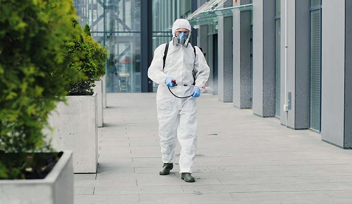 An expert in a hazmat suit spraying disinfectant on a sidewalk walkway