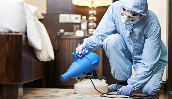 Technician in protective suit fogging under bedroom furniture