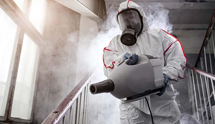 Technician in protective suit using fogging machine on staircase