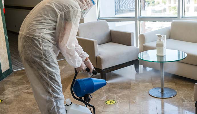 Worker in protective suit fogging commercial lounge floor