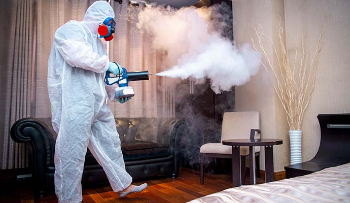 Worker in protective suit fogging room with dense mist