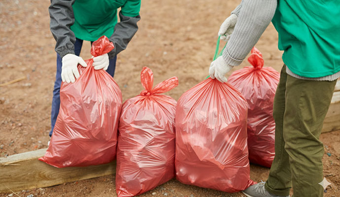 Trauma scene cleaners collecting outdoor waste in red disposal bags