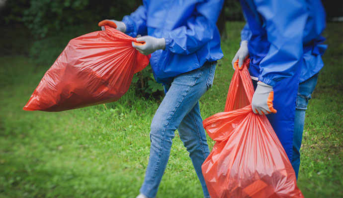 Two professional in blue jackets and protective gloves carrying heavy red plastic bags