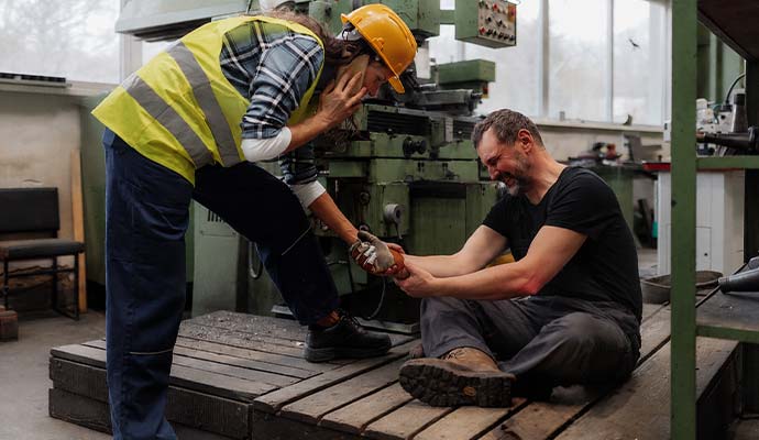 Injured factory worker holding wrist near machinery
