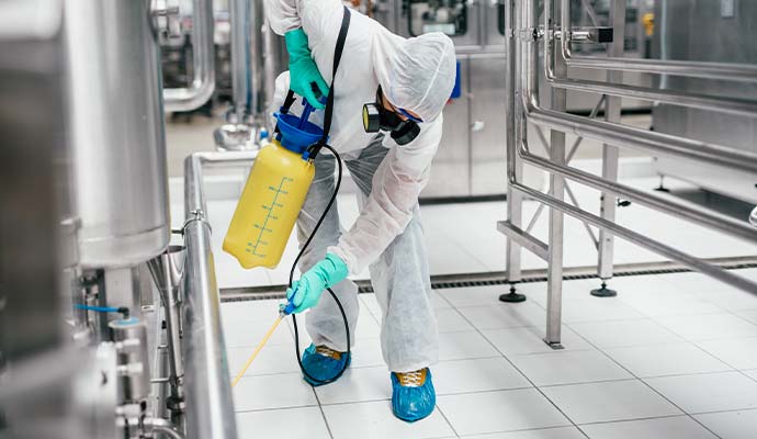 Technician spraying disinfectant around industrial machinery and pipes
