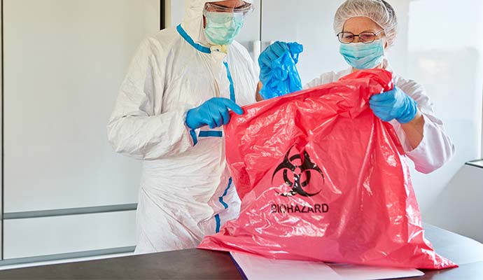 Workers in protective gear holding red biohazard bag