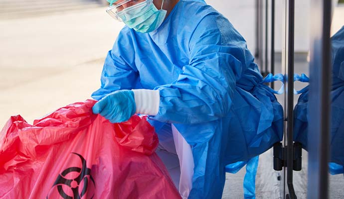 Worker in protective gear holding red biohazard bag