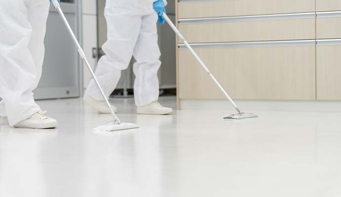 Workers in protective suits mopping floor with flat mops